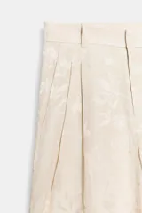 Pantalón de tiro medio confeccionado en hilatura con lino, con cintura con trabillas, bolsillos laterales ocultos y pierna ancha. Presenta un diseño con estampado jacquard de motivos florales en tonos beige y crudo, y cierre frontal con cremallera, botón y ganchos metálicos.