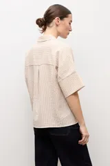 Camisa de manga corta con diseño a rayas en tonos beige y blanco, cuello camisero y cierre frontal con botones ocultos.