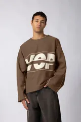 Buzo oversize de algodón rústico color marrón, con diseño boxy, cortes con bordes crudos y estampa frontal con letras blancas.