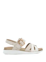 Sandalias planas de mujer en color beige, con tiras cruzadas en el empeine, una de ellas con textura plateada brilhante. Cuenta con tira ajustable al tobillo mediante hebilla con efecto carey y suela blanca con base dentada.