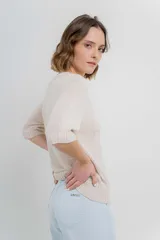 Buzo de tejido abierto color beige claro, de calce oversize con mangas 3/4 y cuello redondo. Presenta terminaciones acanaladas en puños y cintura.