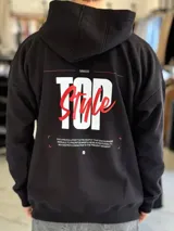 Canguro negro de corte oversize con capucha, manga larga y bolsillo tipo canguro al frente. En la espalda presenta un gran estampado gráfico con las palabras "Top Style" en blanco y rojo, acompañado de inscripciones y detalles minimalistas.