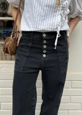 Jean negro de corte wide leg, confeccionado en denim con elasticidad. Presenta tiro alto, cierre frontal con múltiples botones metálicos a la vista y bolsillos delanteros aplicados con detalles bordados.