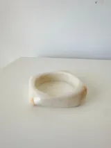 Pulsera rígida de acrílico con diseño asimétrico y acabado marmolado en tonos crema y beige.