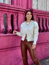 Suéter de punto color crema, con cuello redondo, manga larga y cierre frontal parcial que deja ver parte del abdomen.