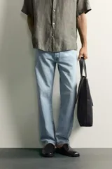 Jeans regular fit de mezclilla negra con efecto lavado, corte recto y tiro medio. Cuenta con diseño de cinco bolsillos y cierre frontal con cremallera y botón.