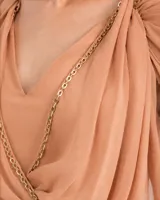 Vestido corto de gasa color durazno, con escote en V, drapeados en el frente y detalle de cadena dorada. Presenta mangas cortas tipo capa y cintura elástica con falda fluida.