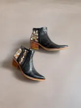 Botas de caña corta de cuero vacuno negro con diseño texturizado tipo cocodrilo y detalles pintados a mano en tonos dorados y blancos en el talón. Cuenta con cierre lateral y taco cuadrado de madera.