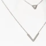 Collar doble plateado con cadena fina. El collar más corto tiene un dije triangular con un pequeño cristal en el centro. El collar más largo tiene un dije en forma de V.