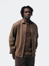 Camisa de manga larga en color marrón, confeccionada en tejido de algodón, con cuello clásico, cierre frontal de botones y un bolsillo en el pecho.