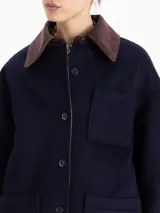 Chaqueta reversible de corte recto. Un lado confeccionado en paño azul marino con cuello de corderoy color chocolate, bolsillos frontales y cierre de botones. El lado interno está realizado en nylon color verde militar.