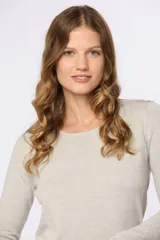 Buzo tejido en hilo de algodón color beige, con cuello redondo y manga larga. Presenta un corte clásico y un pequeño detalle metálico en la parte inferior izquierda.