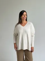 Sweater de punto color beige con escote en V, diseño holgado y costura central vertical. Presenta mangas largas con puños acanalados y ruedo con terminación acanalada.