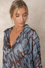 Blusa de gasa con estampado abstracto en tonos verdes y marrones, con detalles de hilos dorados. Presenta cuello camisero con escote en V, mangas largas con puños elásticos y un corte holgado.