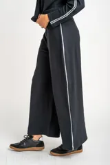Pantalón de corte wide leg color negro, confeccionado en tejido de algodón con elastano. Presenta una franja lateral blanca a lo largo de cada pierna y cintura elástica.