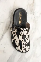 Zueco con capellada de cuero con estampado de vaca en blanco y negro, hebilla metálica plateada ajustable y suela track negra.