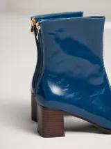 Botas de cuero color marrón con caña media y punta cuadrada. Presentan un cierre trasero, tirador para calzar fácilmente y bordado en color contrastante en el empeine. Suela de goma y taco de madera de 6 cm de altura.