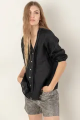 Camisa de lino color negro, con cuello en V, cierre frontal con botones y detalle de alforzas verticales. Presenta mangas tres cuartos con terminación elástica y costuras a contratono.