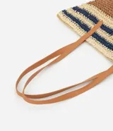 Bolso tipo tote de paja tejida con diseño de rayas horizontales en color natural, marrón y azul marino. Posee asas de hombro en cuero sintético color camel y un dije metálico circular en el frente.