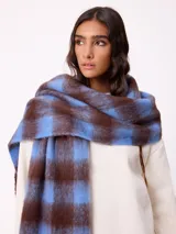 Bufanda de tejido suave con diseño de cuadros grandes en tonos naranja, rojo, violeta y lila. Presenta flecos en los extremos y una etiqueta pequeña con el logo de la marca Rusty.