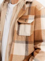 Sobrecamisa de franela con diseño a cuadros en tonos beige y marrón, con capucha integrada de color beige, cierre frontal de botones y bolsillos en el pecho.