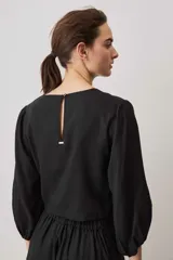 Blusa negra con detalles de apliques bordados en el pecho y las mangas, cuello redondo y mangas largas abullonadas.