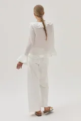 Blusa blanca de gasa con lunares, escote en V con volados y mangas largas acampanadas.