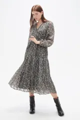 Vestido midi de corte evasé con estampado animal print en tonos blanco y negro. Presenta escote en V cruzado, mangas largas con puños y falda con volados escalonados.
