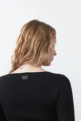 Top de tejido acanalado negro, con escote en V, mangas largas con terminación acampanada y ajuste al cuerpo.