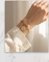 Pulsera de cadena de eslabones gruesos con baño de oro, cierre tipo barra con perla y dije circular con relieve de ángel.
