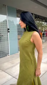 Vestido largo de corte recto y sin mangas, con cuello alto y una abertura lateral pronunciada en la falda. Presenta una textura suave tipo gamuza en color verde oliva.
