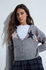 Cardigan corto tejido en color gris, con escote en V y cierre frontal de botones. Presenta un diseño estampado con estrellas y líneas geométricas en tonos oscuros y rojizos, con mangas largas y puños acanalados.