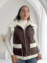 Chaleco marrón de ecocuero con interior de corderito blanco, cierre frontal con cremallera y bolsillos laterales.