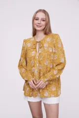 Blusa marrón con estampado de flores color naranja y blanco, con cuello redondo con abertura y mangas largas abullonadas.