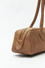 Cartera baguette cilíndrica con estampado de piel de serpiente en tonos beige y negro. Asas cortas y cierre superior con cremallera.