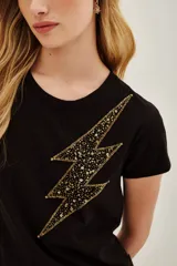 Remera negra de manga corta con cuello redondo y un aplique grande en forma de rayo. El rayo está decorado con lentejuelas doradas y negras.