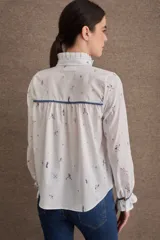 Camisa de popelina blanca con estampado de motivos deportivos, cuello alto con volados, cierre frontal con botones y mangas largas con puños elásticos y volados.
