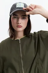 Gorra color gris con efecto acid wash, visera curva y parche frontal bordado con letras y diseño geométrico en tonos amarillo y celeste.