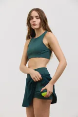 Pollera deportiva corta color verde inglés, con calza incorporada que incluye bolsillo invertido para pelotas. Posee cintura ancha de tiro alto y tejido elastizado de secado rápido.