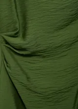Vestido corto de color verde, confeccionado en tejido de modal con textura. Presenta un diseño entallado con cuello drapeado, sin mangas y detalle de drapeado lateral en la cintura. Incluye cierre de cremallera en la parte posterior.