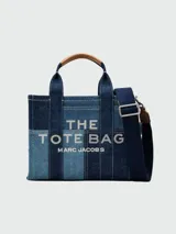 Cartera tipo tote de Marc Jacobs, confeccionada en denim con diseño de paneles en diferentes tonos de azul. Presenta el logo de la marca estampado en el frente, asas superiores de mano y una correa de hombro ajustable y extraíble en color azul oscuro.