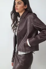 Chaqueta de cuero sintético efecto lavado en color marrón, de corte recto, con cuello camisero, cierre frontal de cremallera metálica y bolsillos laterales.