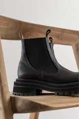 Botas tipo chelsea de cuero negro con textura granulada, paneles laterales elásticos y suela track robusta de goma.