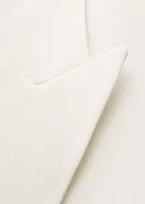 Blazer de corte recto y estilo sastre, color blanco, con cuello de solapa, cierre frontal de botón oculto y bolsillos laterales de ribete.