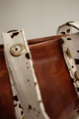 Cartera grande de cuero color marrón con asas de cuero con estampado animal print y ojales dorados.