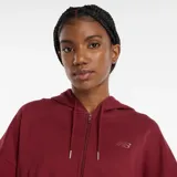 Campera con capucha y cierre frontal, color rojo oscuro (bordó), de corte cropped y calce holgado. Presenta un pequeño logo de New Balance bordado en el pecho izquierdo.