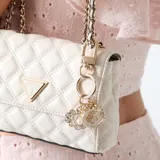 Llavero Guess de aleación dorada con múltiples dijes colgantes, incluyendo una flor esmaltada en blanco con perla central, la letra G revestida de cristales y un corazón metálico con grabado de la marca.
