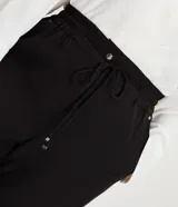 Pantalón de corte fluido y estilo pijama, color negro, con cintura elástica ajustable mediante lazo y detalle de tiras con hebilla en los tobillos.