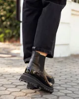 Botinetas tipo Chelsea de cuero negro, con paneles laterales elásticos y suela track dentada de goma. Presentan una combinación de texturas entre cuero mate y cuero charolado en la puntera y el talón.