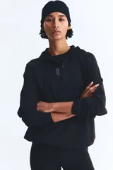 Campera deportiva de running color negro, confeccionada en tejido funcional DryMove. Presenta un diseño de corte holgado con medio cierre frontal, capucha de doble capa, mangas raglán con abertura para el pulgar y bolsillos laterales con cierre. Incluye cordón elástico ajustable en el bajo y detalles reflectantes.